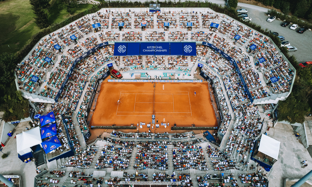 Luftaufnahme eines überfüllten Tennisstadions mit Sandplatz und Spielern mitten im Spiel während eines Turniers.