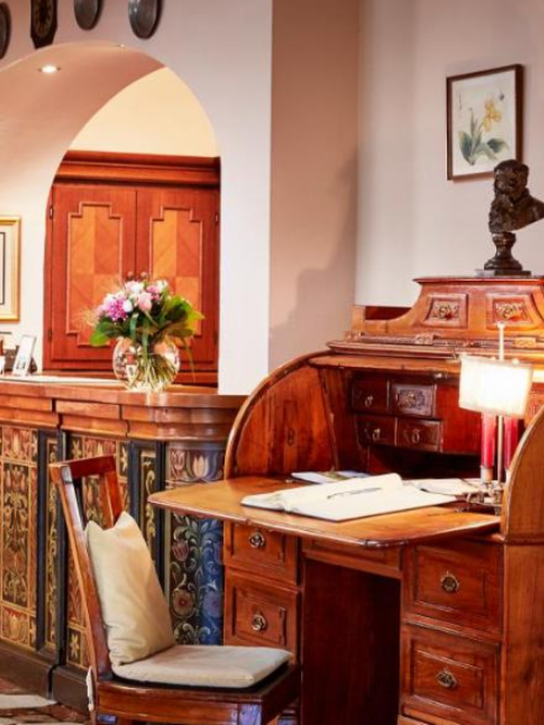 Verschnörkelter Holztisch mit Papieren, ein Stuhl, frische Blumen und dekorative Kunstwerke in einem gemütlichen Raum.