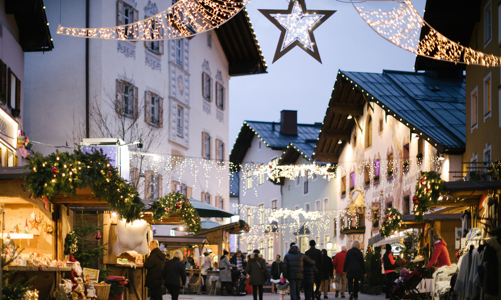 Ein festlicher Straßenmarkt mit Lichtern und Dekorationen, Menschen, die spazieren gehen, und Ständen, die Weihnachtsartikel verkaufen.