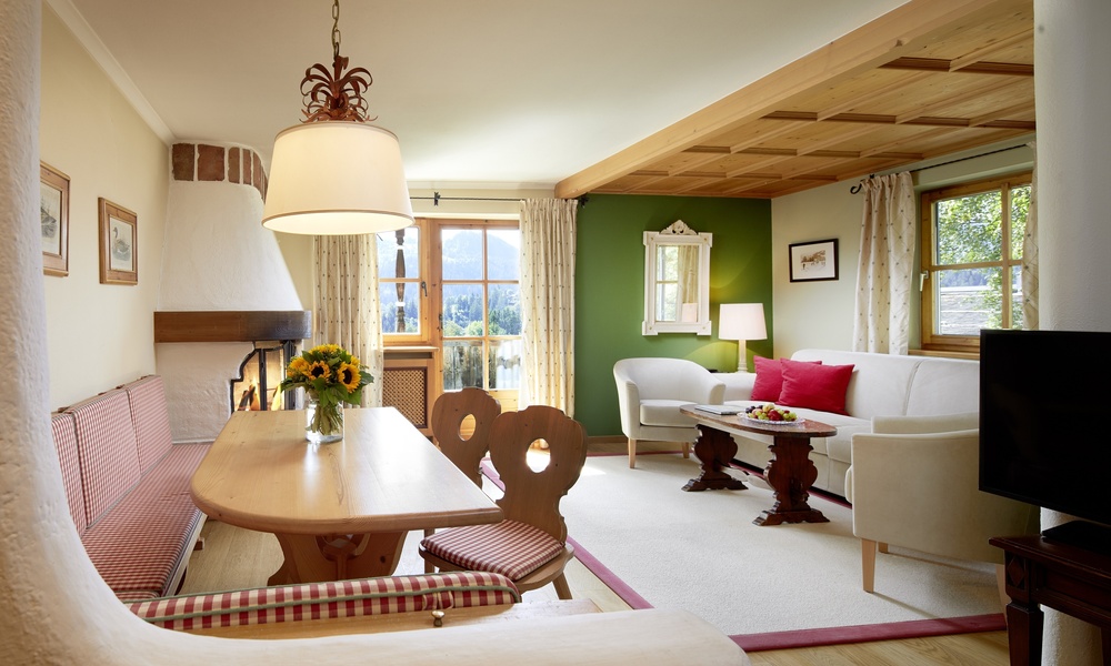 Gemütlicher Wohn- und Essbereich mit Holzmöbeln, Kamin, großen Fenstern und Sonnenblumen auf dem Tisch.