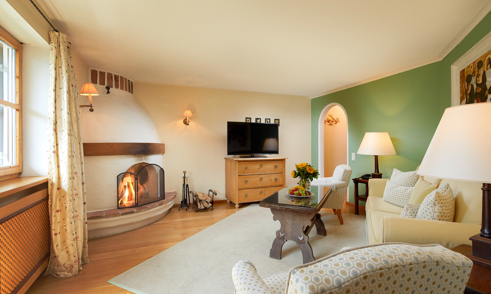 Gemütliches Wohnzimmer mit beleuchtetem Kamin, Fernseher auf einer Kommode, grüner Akzentwand und bequemen Sitzgelegenheiten.