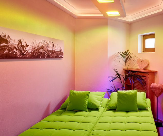 A cozy room with a green bed, two green pillows, warm lighting and mountain art on the wall.