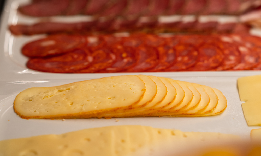 Geschnittener Käse und verschiedene Wurstsorten auf einer weißen Platte angerichtet.