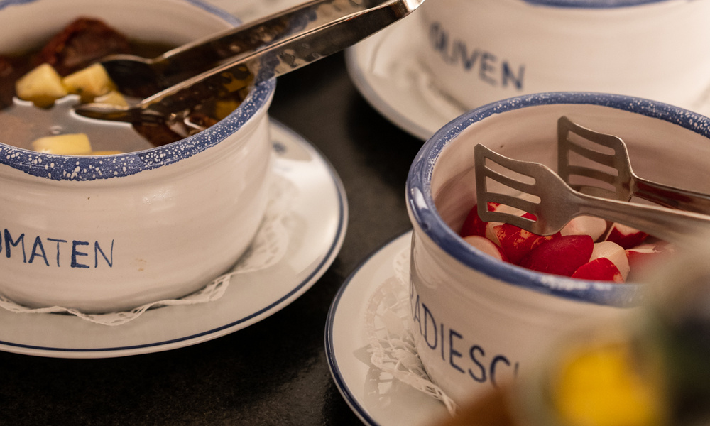 Nahaufnahme von Keramikschalen mit Lebensmitteln und Servierzange, eine Schale gefüllt mit geschnittenen Radieschen.