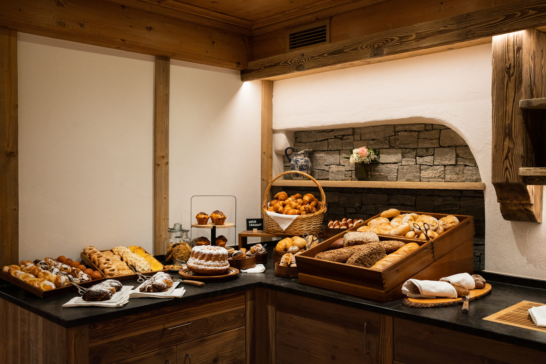 Various types of bread and baked goods are offered on a wooden counter in a rustic bakery.