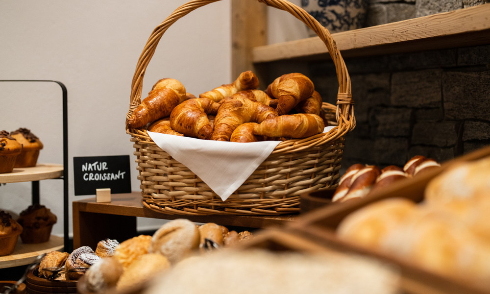 Ein mit Croissants gefüllter Weidenkorb steht in einem Bäckereiregal neben anderem Gebäck.
