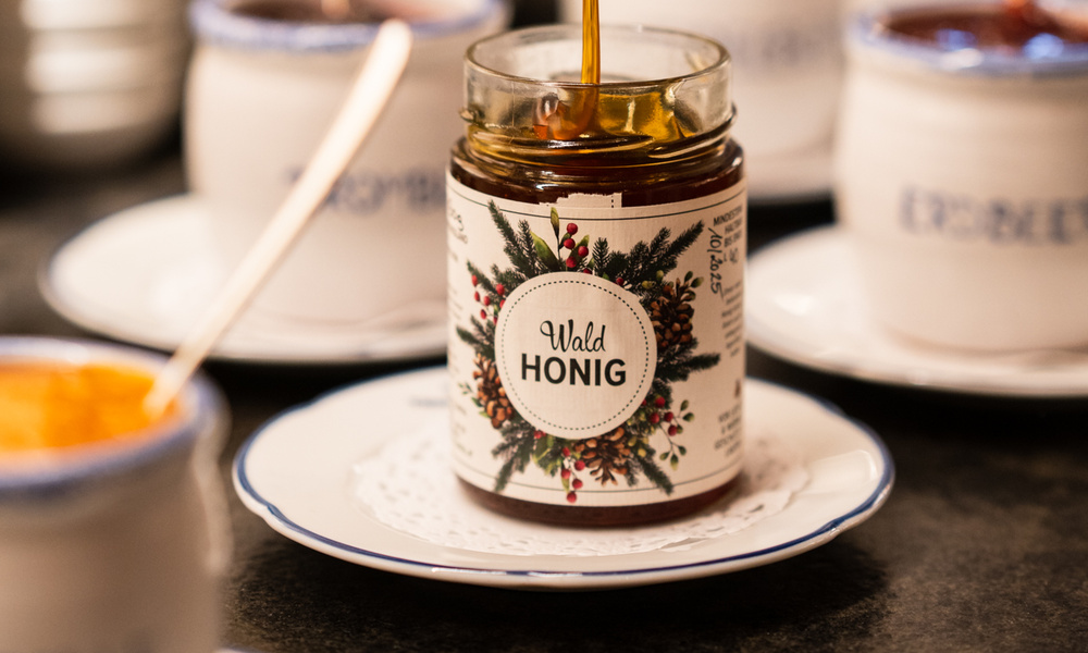 Ein Glas Waldhonig mit eingefülltem Honig, umgeben von Porzellangefäßen.