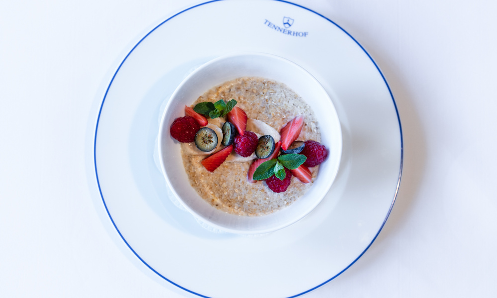 Eine Schüssel Haferflocken mit Beeren und Minzblättern auf einem weißen Teller mit blauem Rand.