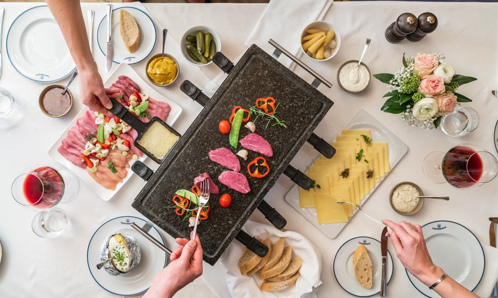 Ein für eine Mahlzeit gedeckter Tisch mit rohem Fleisch, Käse, Gemüse, Brot und einem heißen Steingrill in der Mitte.