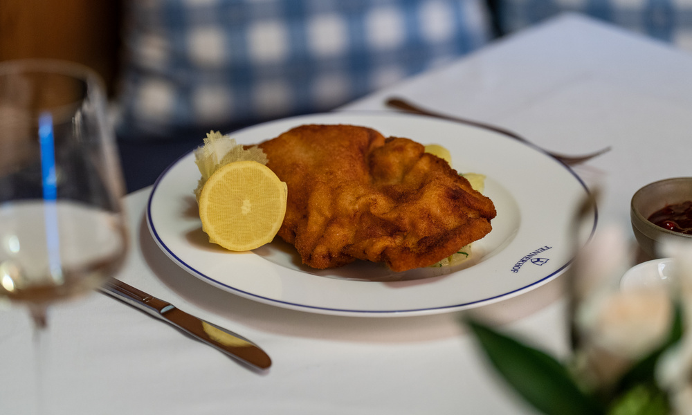 Ein Teller mit paniertem Schnitzel und einer Zitronenspalte auf einem weißen Tischtuch, gedeckt zum Essen.