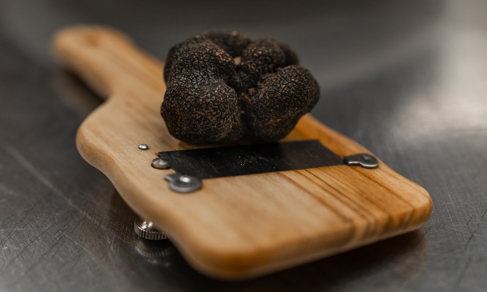 Eine schwarze Trüffel, die auf einem hölzernen Trüffelhobel auf einer Metallfläche ruht.