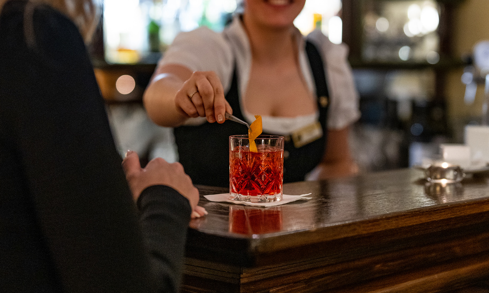 Ein Barkeeper garniert einen Cocktail für einen Kunden in einer schummrigen Bar.