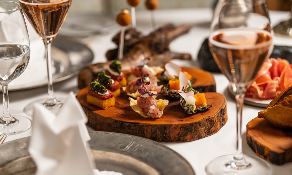 Ein Holztablett mit verschiedenen Vorspeisen und Gläsern Roséwein auf einem eleganten Tisch.
