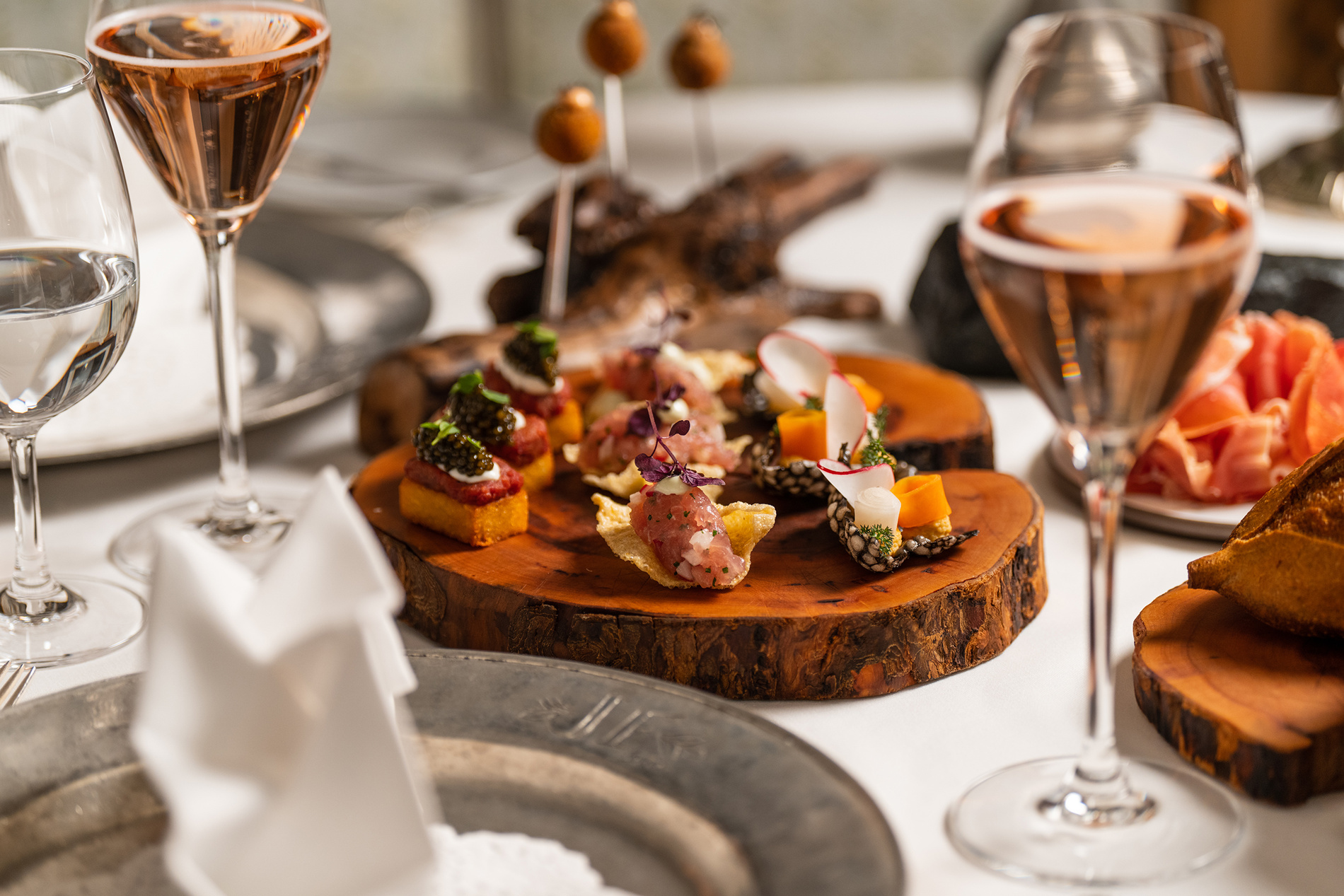 Ein Holztablett mit verschiedenen Vorspeisen und Gläsern Roséwein auf einem eleganten Tisch.