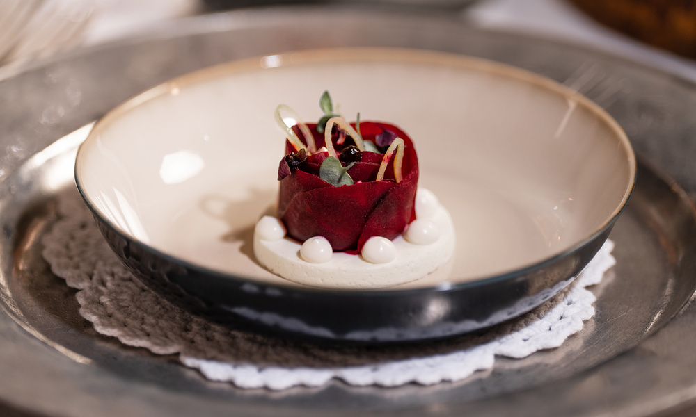 Ein Gourmet-Dessert mit roten Früchten, Sahne und Garnierungen, serviert auf einem weißen Deckchen in einer Keramikschale.