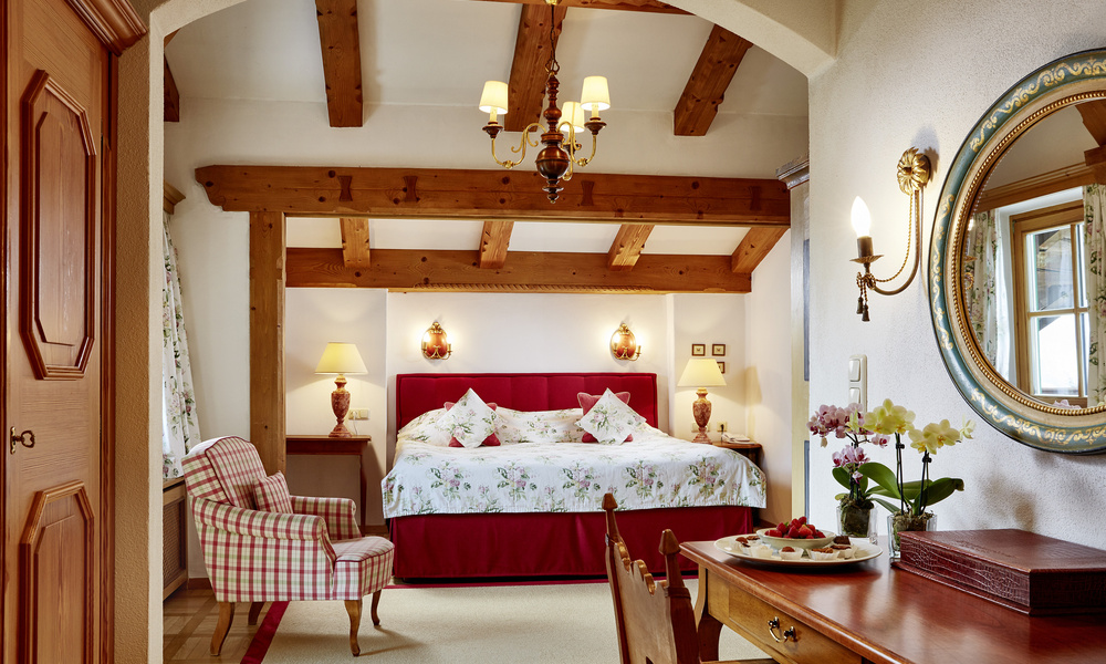 Gemütliches Schlafzimmer mit Holzbalken, geblümter Bettwäsche und eleganter Einrichtung, mit Bett, Stuhl und Schreibtisch.