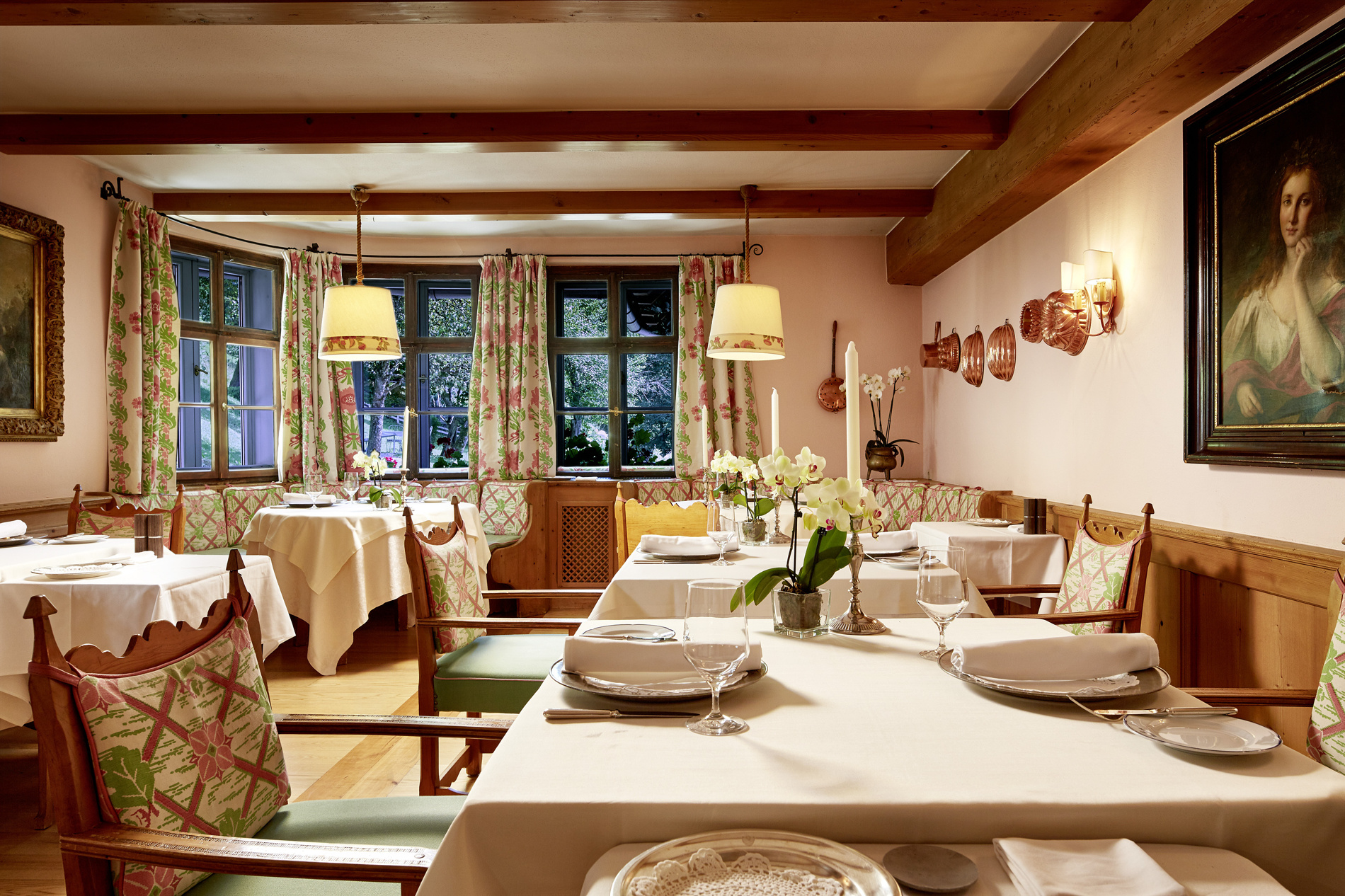 Cozy dining room in the restaurant with flowered curtains, laid tables, wooden chairs and soft pendant lighting.