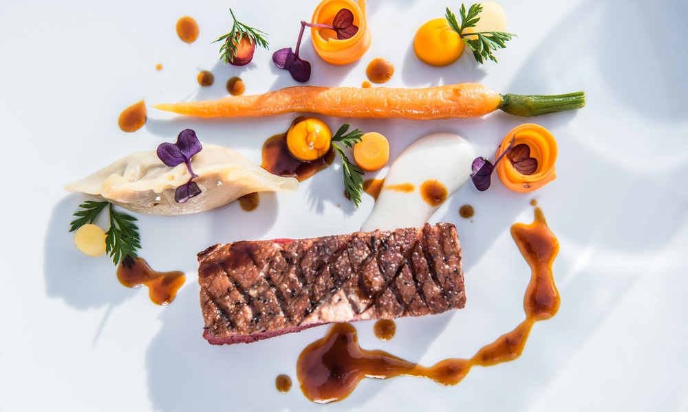 Gourmet-Gericht mit gegrilltem Fleisch, Karotten, Soße, Gemüsebeilagen und kunstvoller Präsentation.