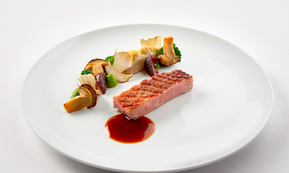 Ein Gourmetgericht mit gebratenem Fleisch, verschiedenen Gemüsesorten und Soße, kunstvoll auf einem weißen Teller angerichtet.