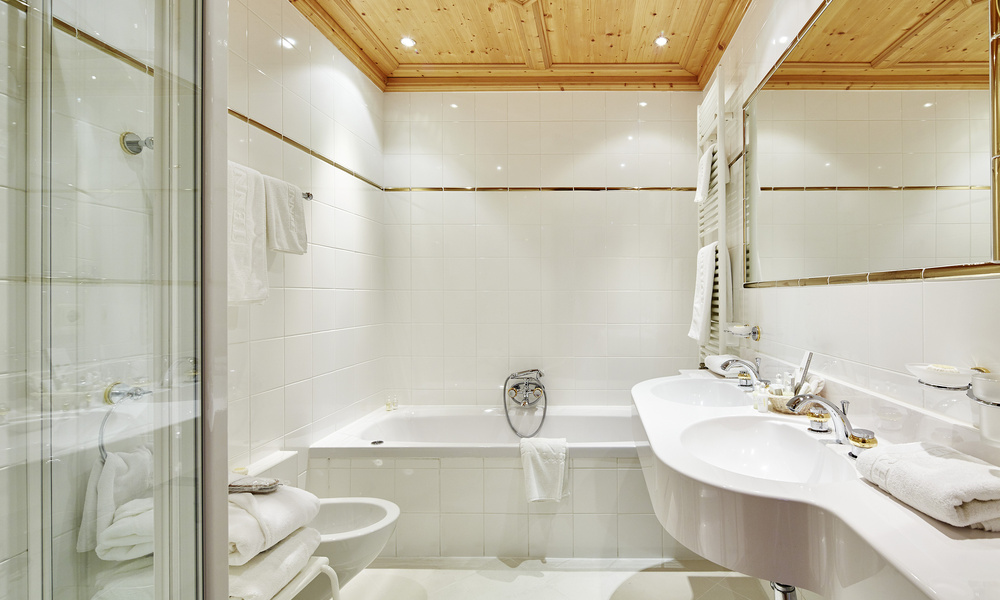 Modernes weißes Badezimmer mit Badewanne, Doppelwaschbecken, großem Spiegel, Handtuchhalter und holzgetäfelter Decke.