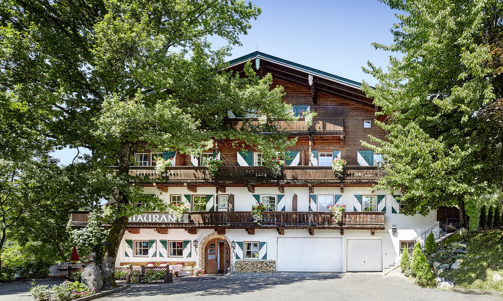 Ein traditionelles Holzchalethotel mit Balkonen, grünen Fensterläden und Bäumen, die das Gebäude umrahmen.