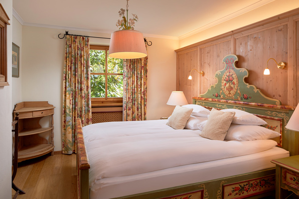 Cozy bedroom with a double bed, floral curtains, wooden furniture and warm lighting.