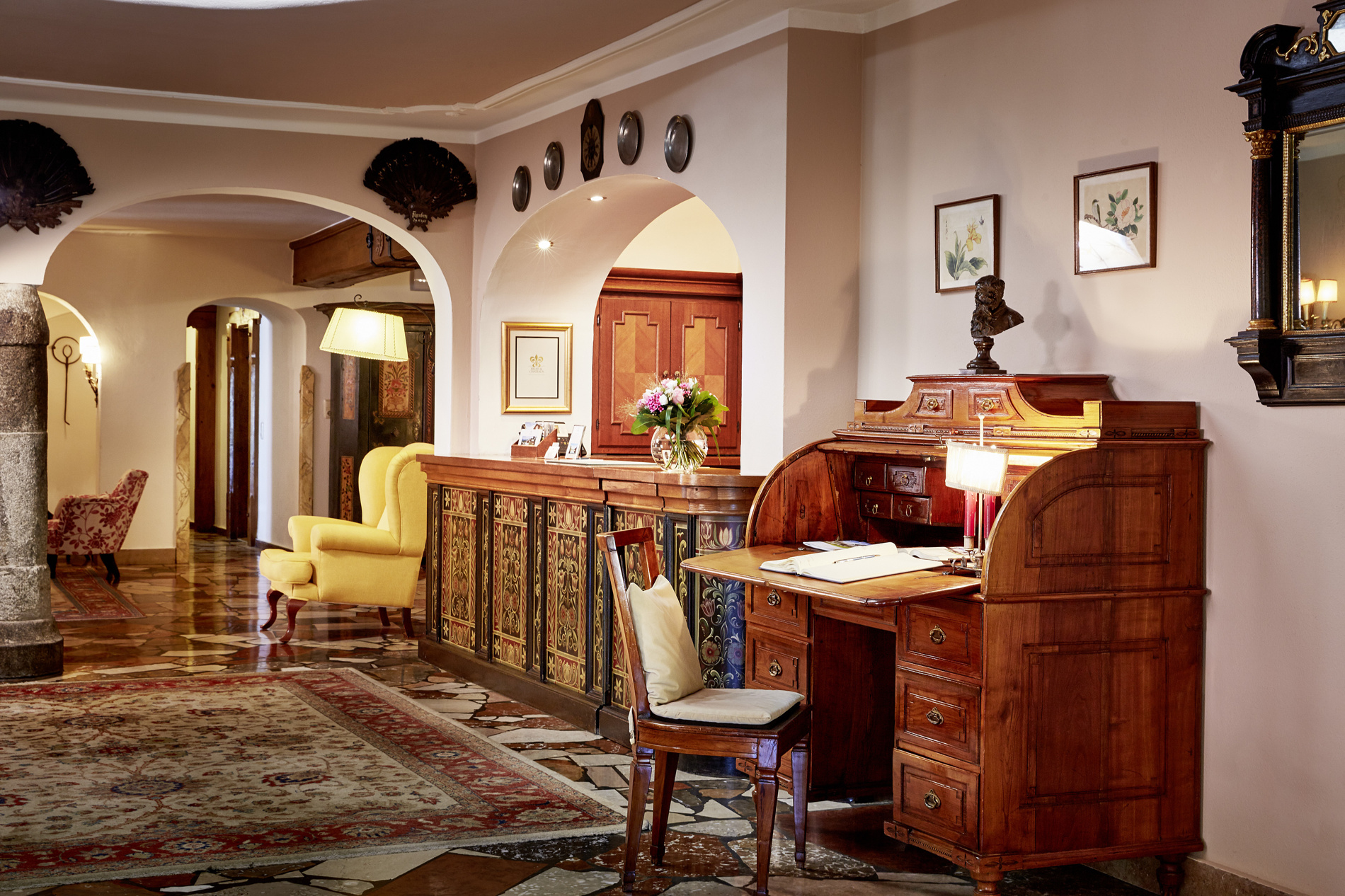 Elegante Hotellobby mit antikem Holztisch, Stuhl, Blumenteppich und klassischem Dekor. Frische Blumen auf dem Tresen.