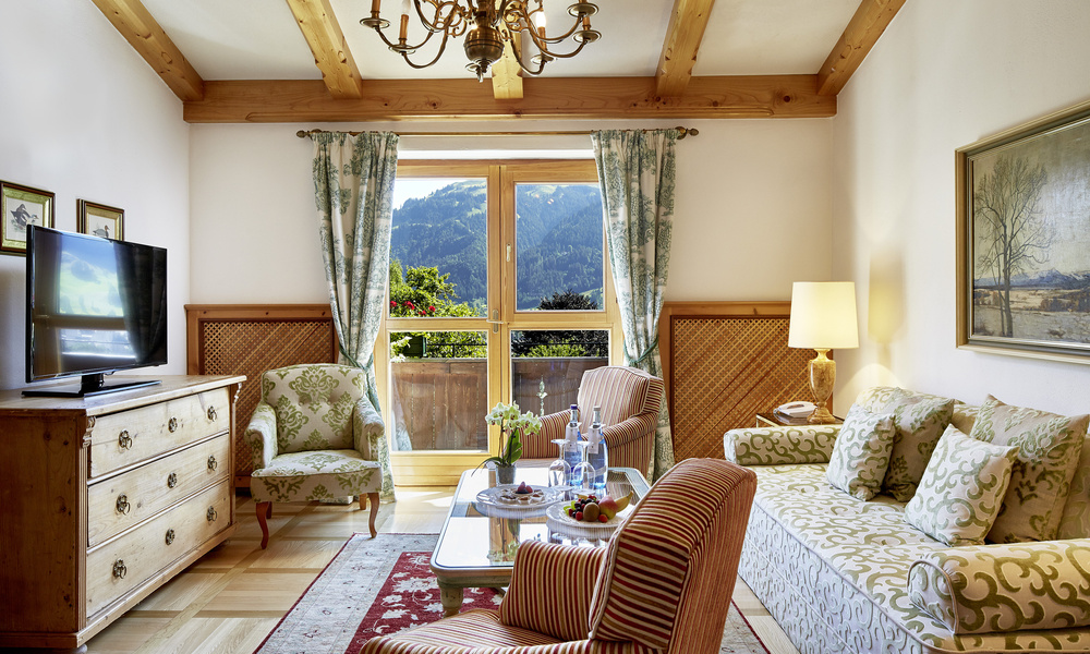 Gemütliches Wohnzimmer mit gemusterten Möbeln, TV, Kronleuchter und Bergblick durch ein großes Fenster.