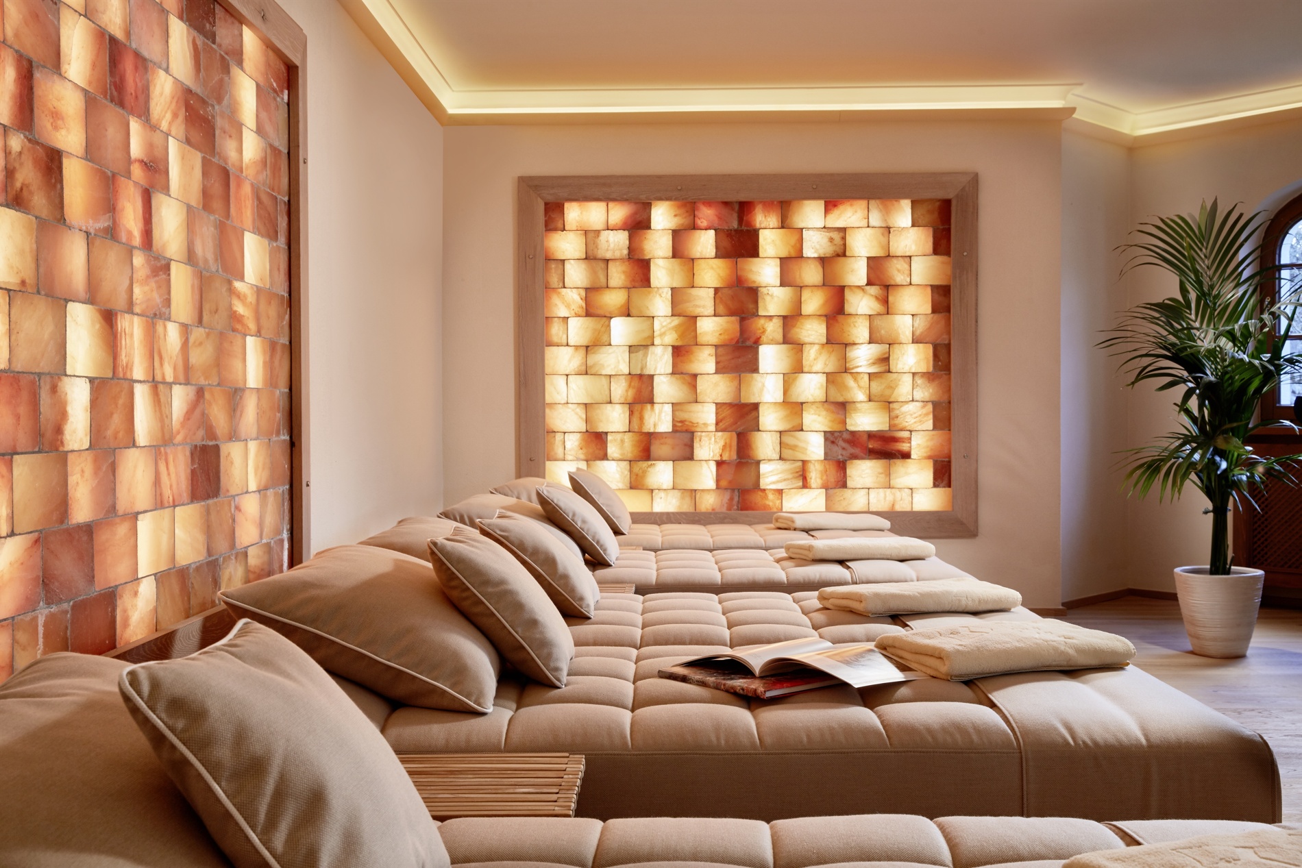 Relaxing spa room with beige lounge beds, luminous salt brick walls, soft cushions and a potted plant.