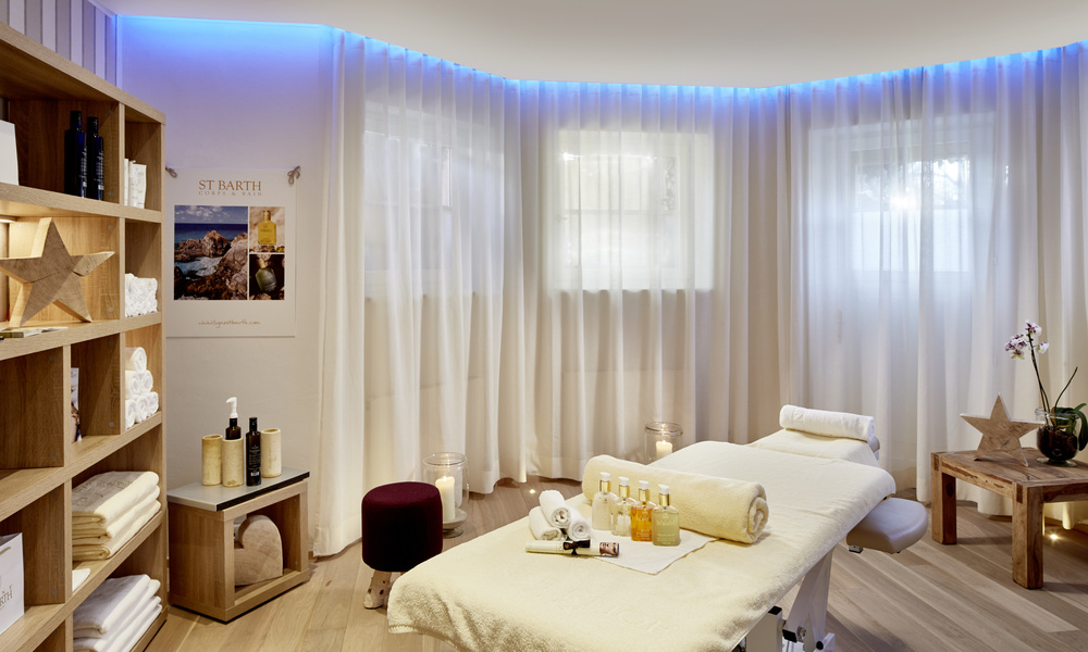 Ein ruhiger Wellness-Raum mit einer Massageliege, sanfter Beleuchtung und Regalen mit Handtüchern und Hautpflegeprodukten.