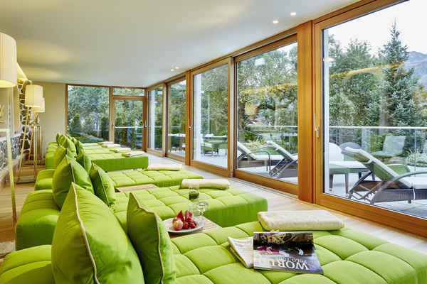 Moderne Lounge mit grün gepolsterten Stühlen an großen Fenstern mit Blick auf einen bewaldeten Außenbereich.