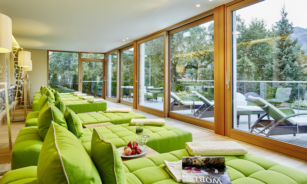 Moderne Lounge mit grün gepolsterten Stühlen an großen Fenstern mit Blick auf einen bewaldeten Außenbereich.
