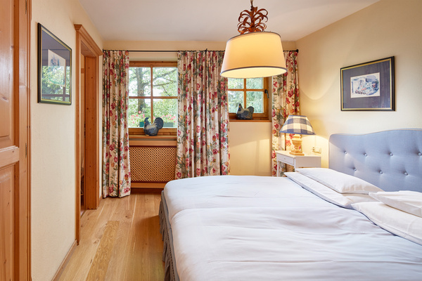 Gemütliches Schlafzimmer mit blauem Bett, geblümten Vorhängen, Holzboden und gerahmten Bildern an den Wänden.