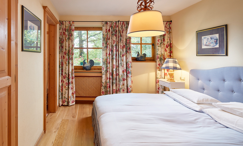 Gemütliches Schlafzimmer mit geblümten Vorhängen, Einzelbetten, Holzboden und sanfter Lampenbeleuchtung.