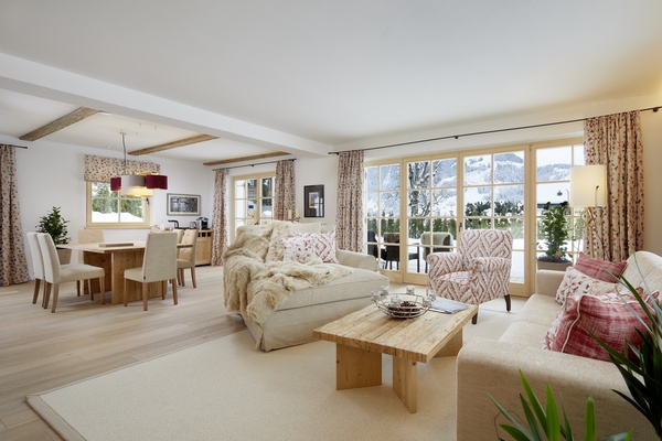 Heller Wohn- und Essbereich mit gemütlichen Sofas, Holztisch, großen Fenstern und Winterlandschaft draußen.