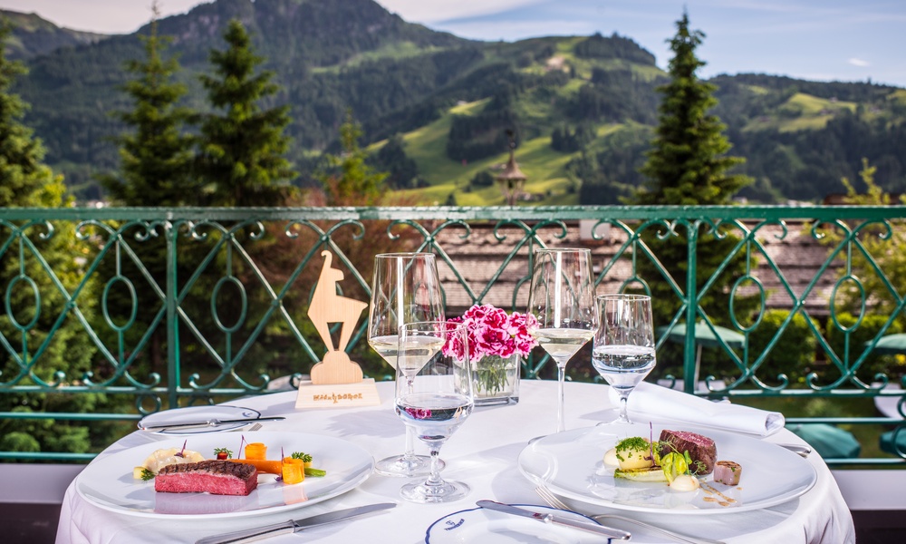 Esstisch im Freien mit Gourmetgerichten, Weingläsern und einer Berglandschaft im Hintergrund.