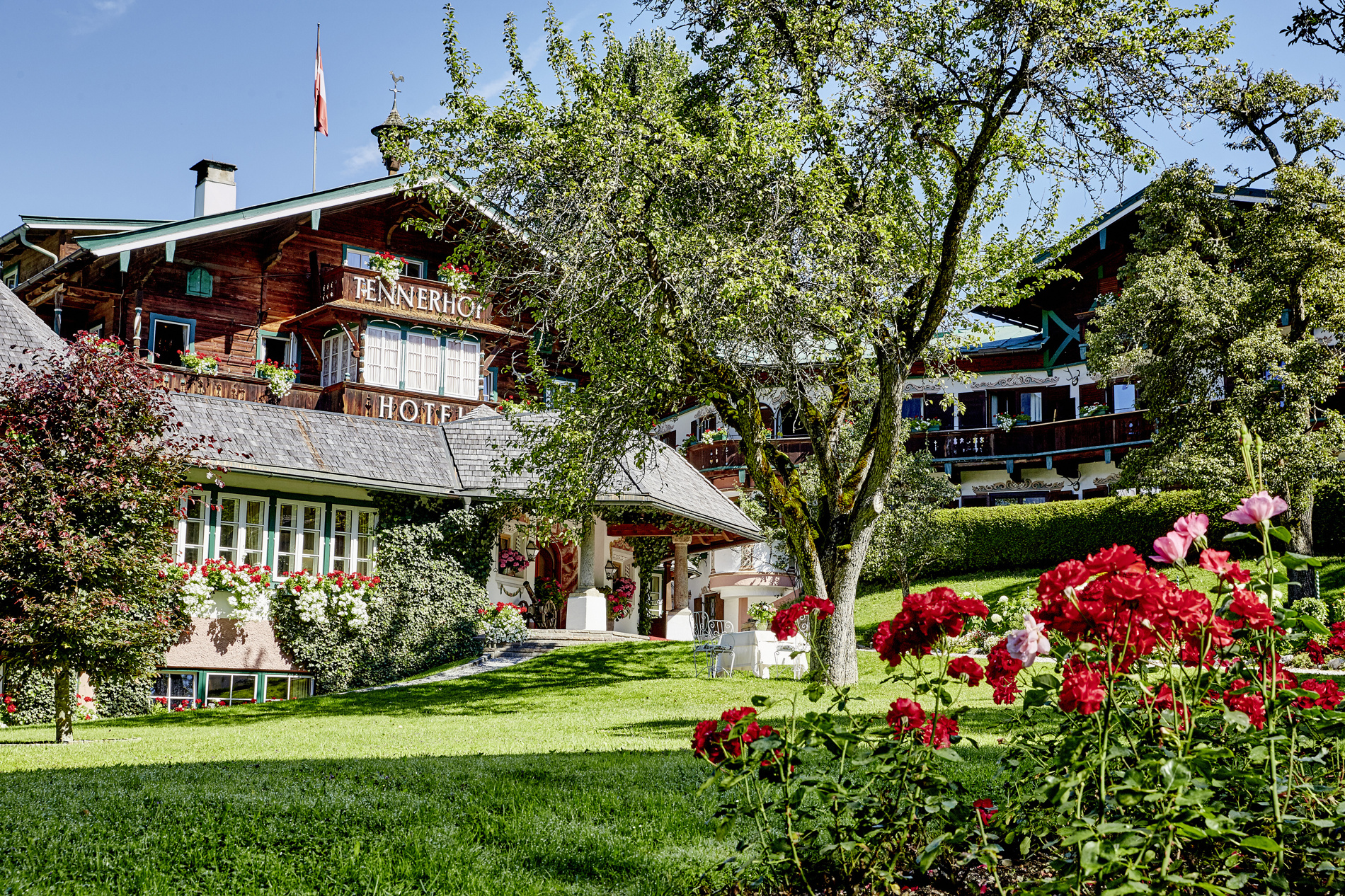 Ein charmantes Hotel mit Holzarchitektur, umgeben von üppigem Grün und blühenden roten Blumen.