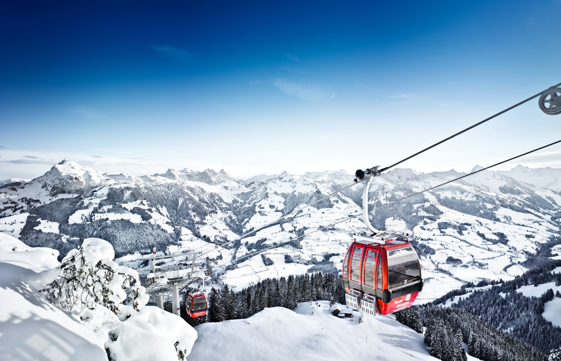 Rote Seilbahnen fahren unter blauem Himmel über verschneite Alpenberge.