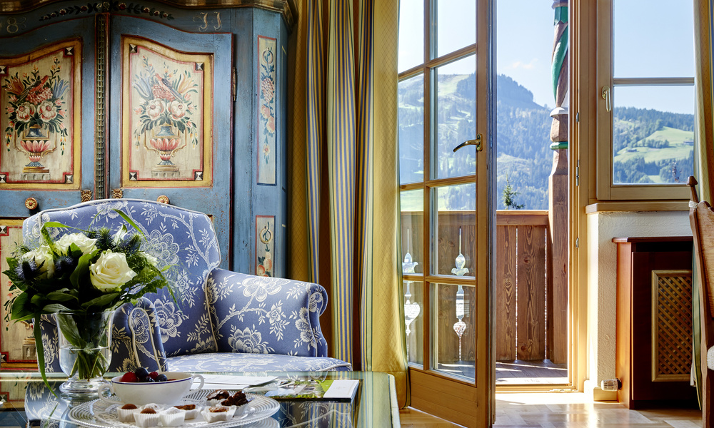 Elegantes Zimmer mit Blumendekor, einem Blumenstrauß auf einem Glastisch und einer Balkontür mit Blick auf die Berge.