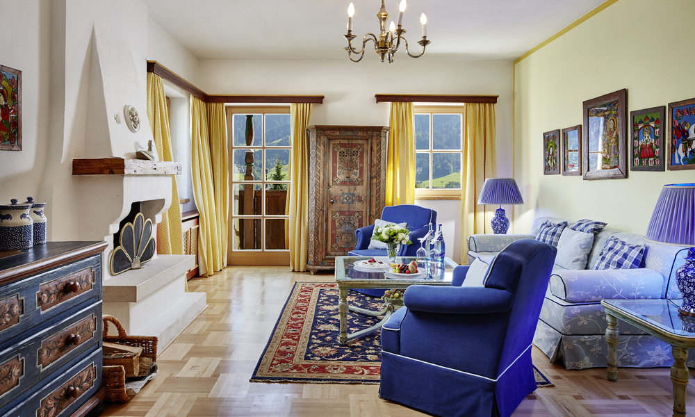 Helles Wohnzimmer mit blauen Möbeln, gelben Vorhängen, Kamin und farbenfroher Dekoration, mit Blick auf die Berge draußen.