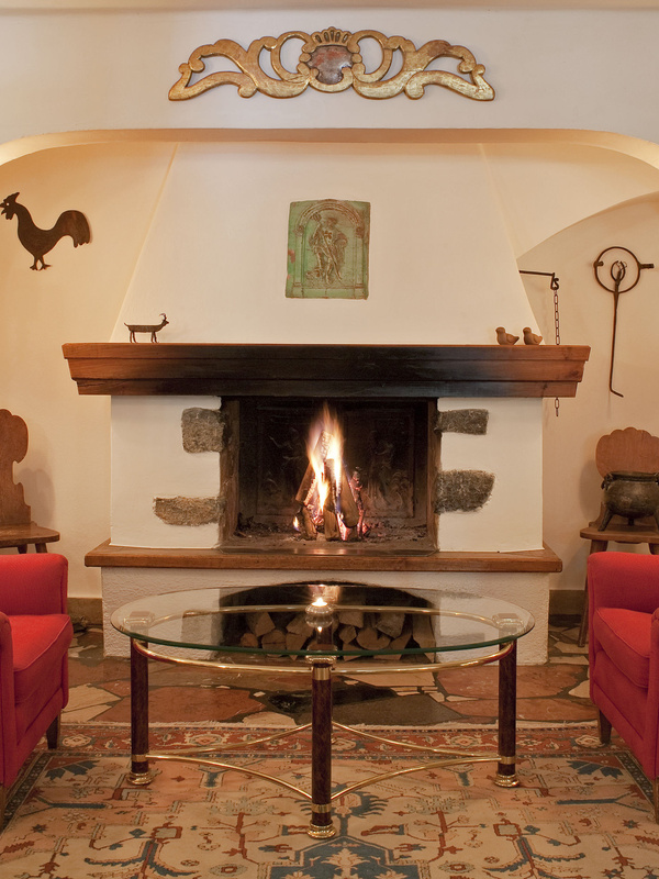 Ein gemütlicher Kamin, in dem ein Feuer brennt, flankiert von roten Stühlen und dekoriert mit rustikaler Kunst und Ornamenten.