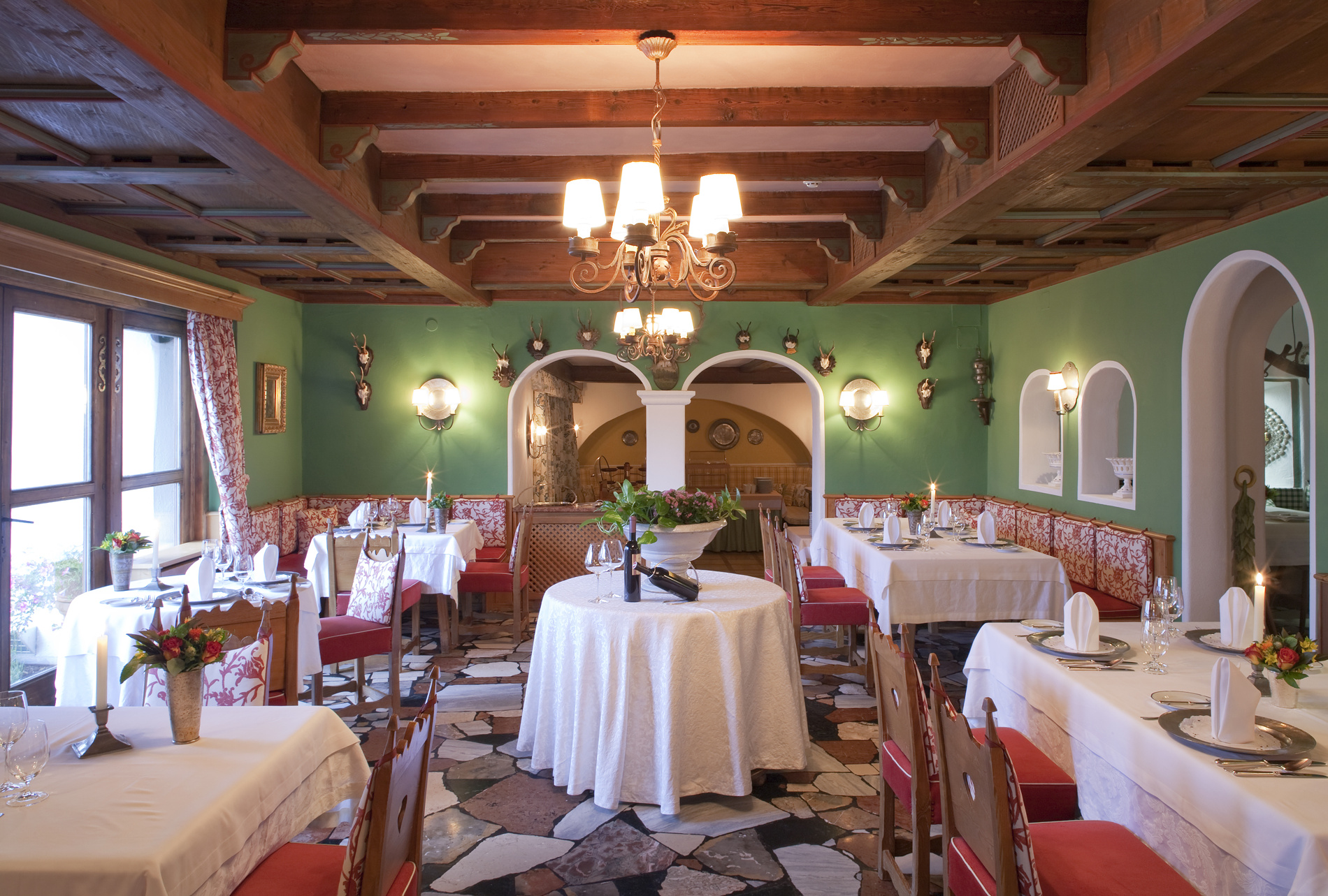 Eleganter Speisesaal eines Restaurants mit Holzdecke, gedeckten Tischen, grünen Wänden und dekorativer Beleuchtung.