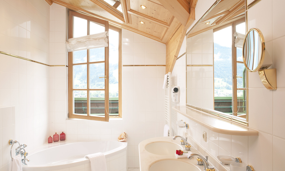 Helles Badezimmer mit runder Badewanne, Doppelwaschbecken, großem Spiegel und Fenster mit Blick auf die Berge.