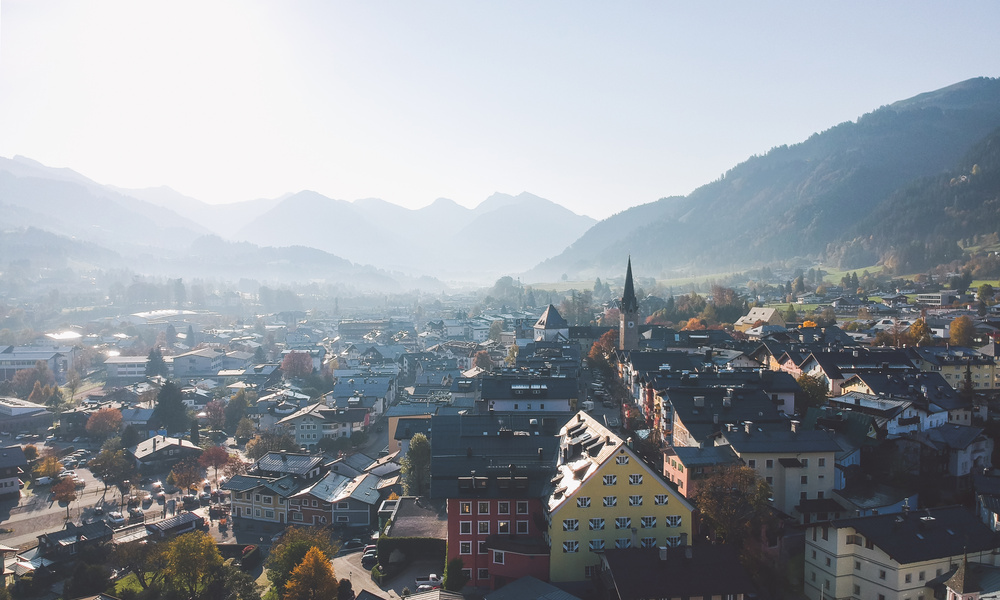 Luftaufnahme einer malerischen Stadt mit bunten Gebäuden, umgeben von nebligen Bergen an einem klaren Tag.