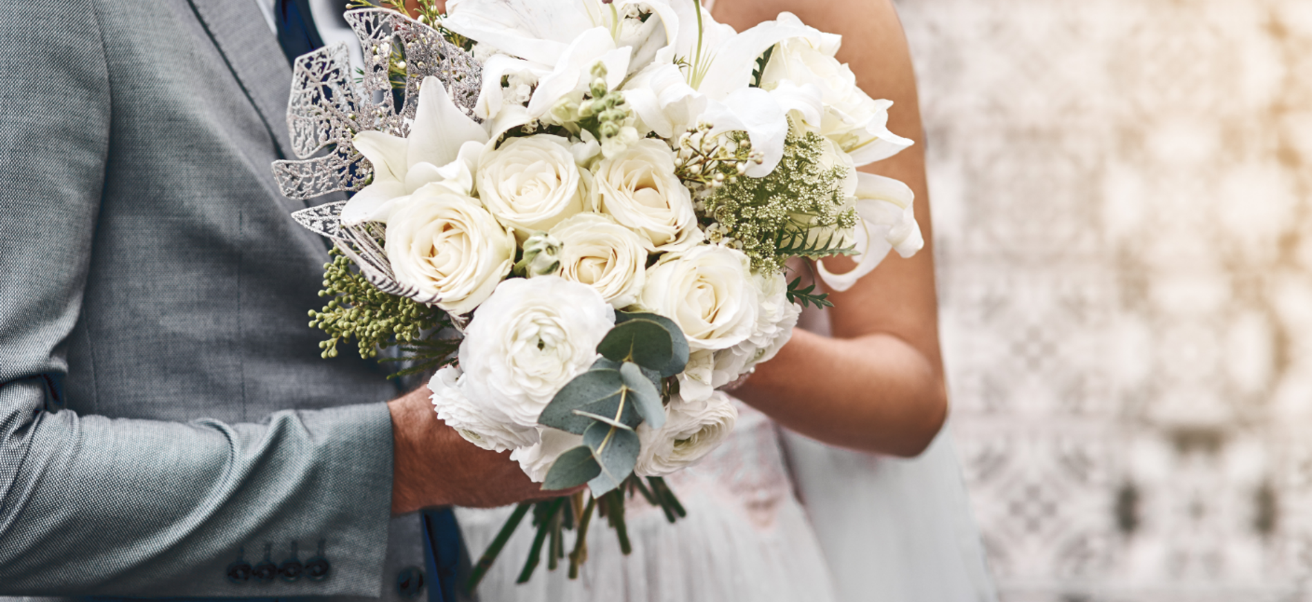 Braut und Bräutigam halten an ihrem Hochzeitstag einen Strauß aus weißen Rosen und Lilien.