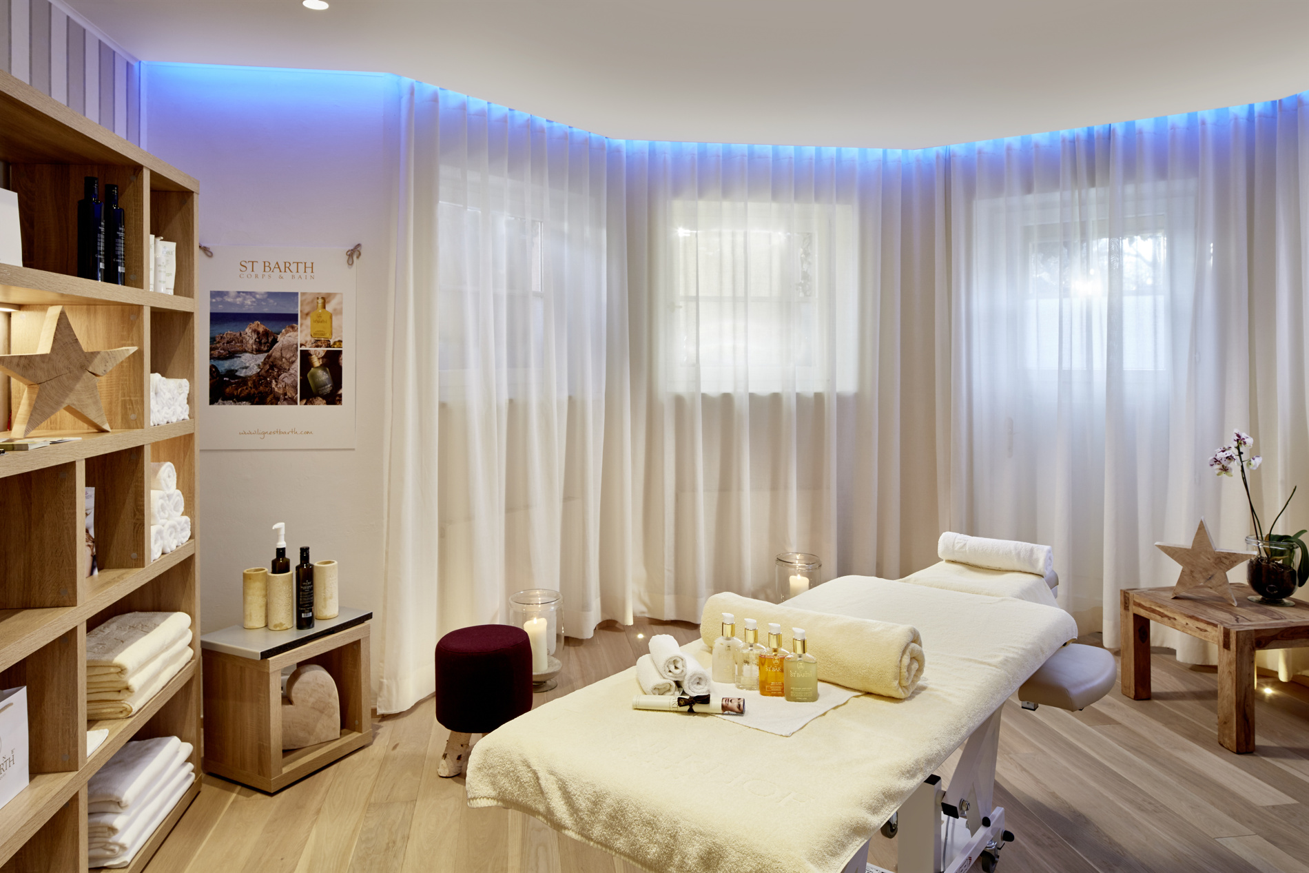 A quiet wellness room with a massage table, soft lighting, shelves with towels and wellness products.