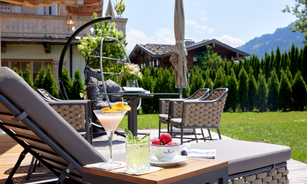 Lounge-Bereich im Freien mit Getränken, Kaffee und Erdbeeren auf einem Tisch, umgeben von Grün und Bergen.