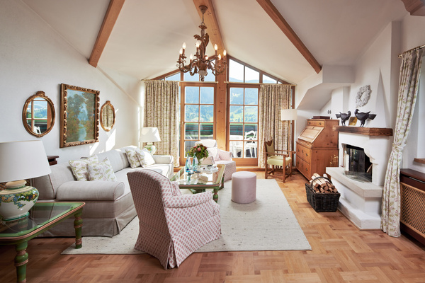 Helles, elegantes Wohnzimmer mit gemütlichen Sitzgelegenheiten, Kronleuchter, Kamin und großen Fenstern mit Blick auf die Berge.