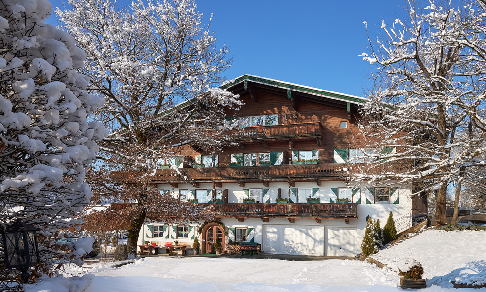 Ein Holzchalet mit Balkonen, umgeben von schneebedeckten Bäumen an einem sonnigen Wintertag.