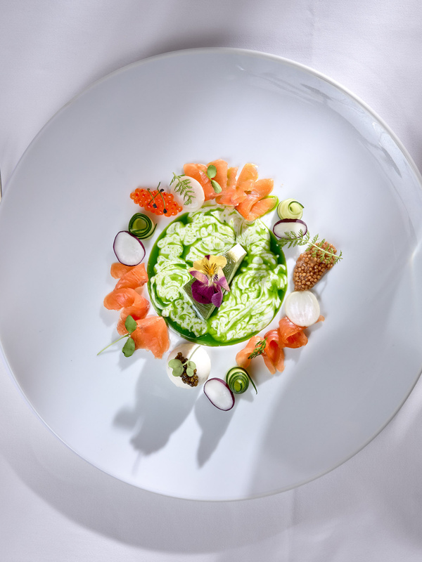 Ein Feinschmeckersalat, kunstvoll angerichtet auf einem weißen Teller mit Besteck und Gläsern auf einem weißen Tischtuch.